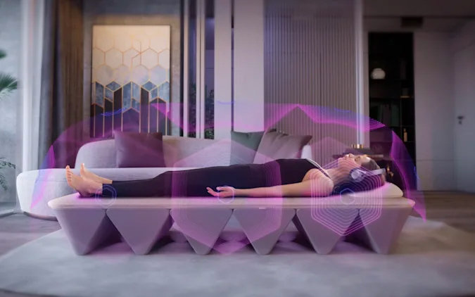 A person lying on the OPUS SoundBed™ with vibrant pink and purple sound waves illustrated, demonstrating the immersive sound therapy experience.