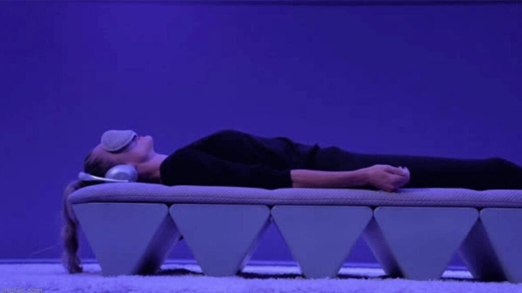 A person lying on the OPUS SoundBed™ in a serene environment with soft purple lighting, experiencing sound therapy.