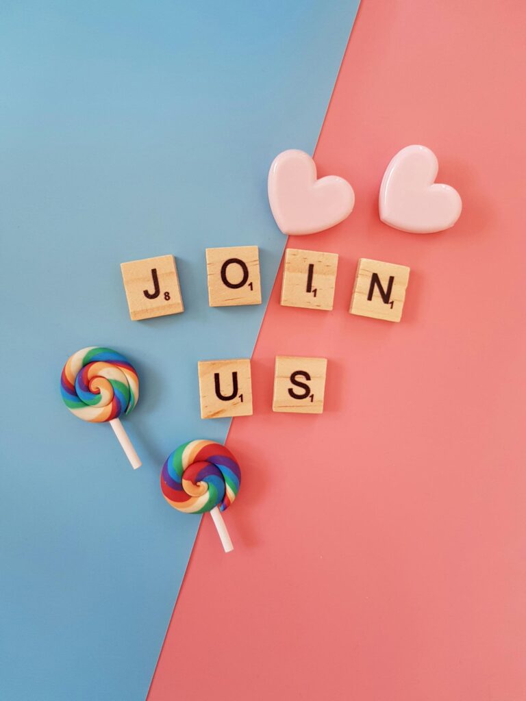 Colorful scrabble tiles spelling 'JOIN US' with heart-shaped decorations and rainbow lollipops on a blue and pink background.